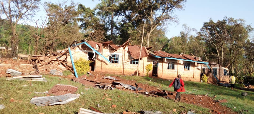 School building with one end derelict and the roof fallen in. A chid with a backpack walks in front.